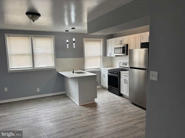 kitchen with a sink, wood finished floors, white cabinetry, appliances with stainless steel finishes, and a peninsula