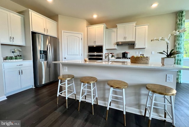 kitchen featuring dark wood finished floors, a sink, white cabinets, under cabinet range hood, and appliances with stainless steel finishes