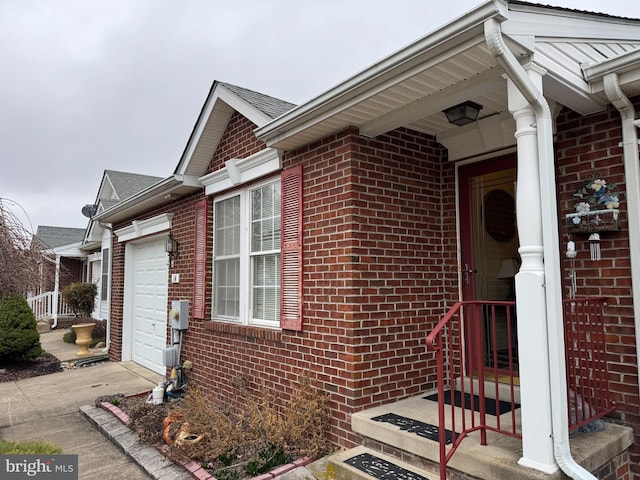 doorway to property with a garage, brick siding, roof with shingles, and concrete driveway