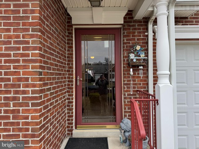 view of exterior entry with a garage and brick siding