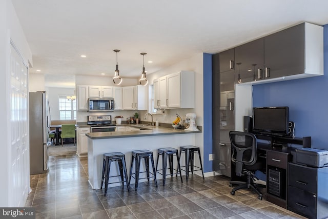 kitchen with a peninsula, a sink, stainless steel appliances, white cabinetry, and a kitchen bar