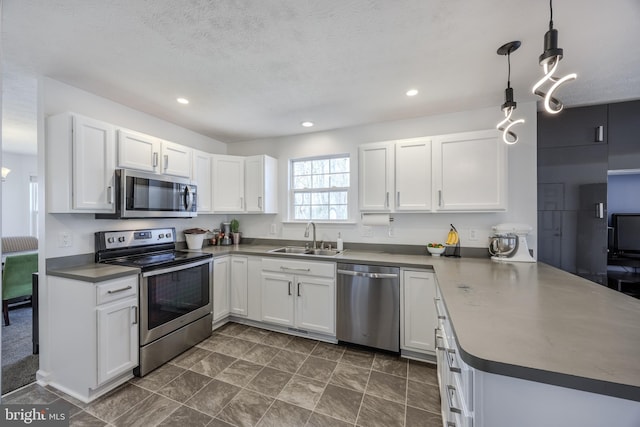 kitchen featuring dark countertops, appliances with stainless steel finishes, a peninsula, white cabinets, and a sink