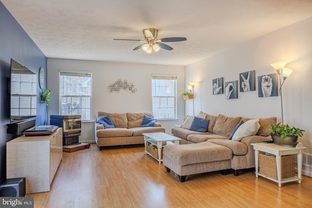 living area with light wood-style flooring, a ceiling fan, a wealth of natural light, and a textured ceiling