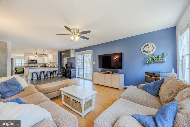 living room featuring plenty of natural light, baseboards, light wood-type flooring, and a ceiling fan