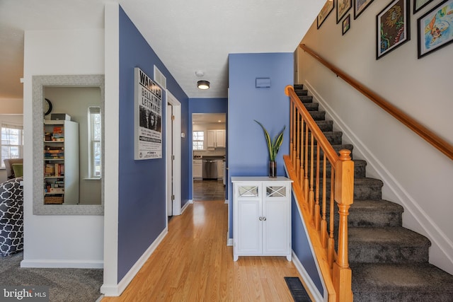 stairway featuring a wealth of natural light, visible vents, baseboards, and wood finished floors