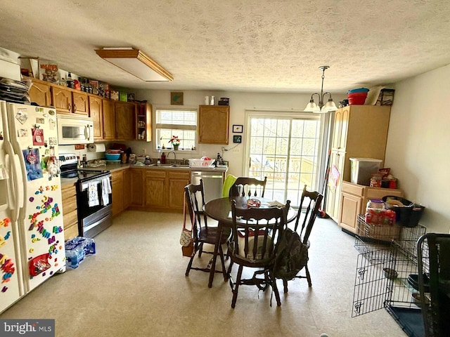 kitchen with white appliances, a sink, pendant lighting, a notable chandelier, and brown cabinets