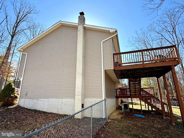 view of home's exterior featuring a chimney, stairs, a deck, and fence