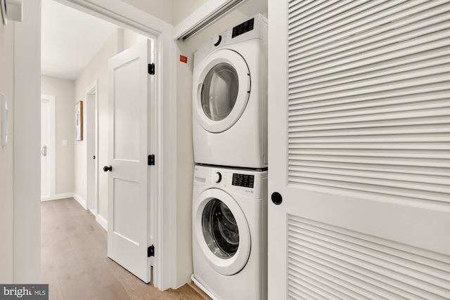 washroom featuring baseboards, stacked washer and clothes dryer, light wood-style flooring, and laundry area