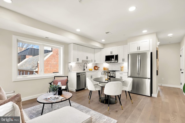 kitchen with a sink, stainless steel appliances, tasteful backsplash, and light wood-style flooring