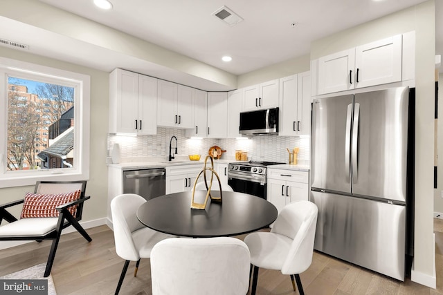 kitchen with decorative backsplash, light wood-style floors, visible vents, and stainless steel appliances