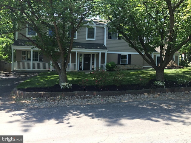 view of front of property with aphalt driveway, stone siding, covered porch, and a front yard