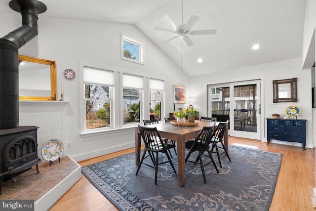 dining room featuring baseboards, a wood stove, wood finished floors, high vaulted ceiling, and a ceiling fan