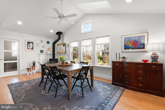 dining room with recessed lighting, light wood-style floors, a skylight, baseboards, and a wood stove