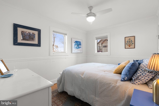 bedroom featuring a wainscoted wall, multiple windows, and ornamental molding