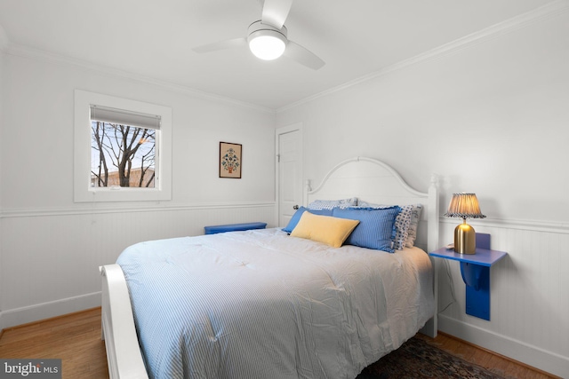 bedroom featuring ceiling fan, crown molding, wood finished floors, and wainscoting