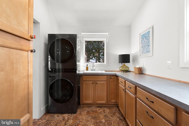 laundry area with stacked washer / dryer, cabinet space, stone finish flooring, and a sink