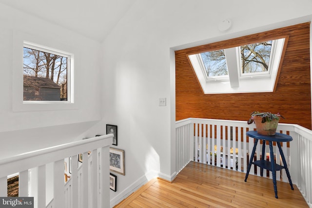 hall featuring light wood-type flooring, an upstairs landing, baseboards, and vaulted ceiling with skylight