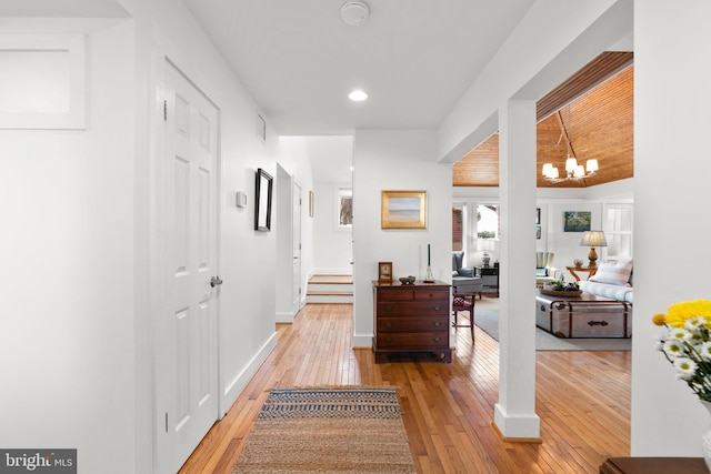 hall featuring light wood-type flooring, baseboards, an inviting chandelier, and stairway