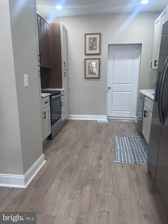 kitchen featuring baseboards, light countertops, electric range oven, wood finished floors, and stainless steel fridge