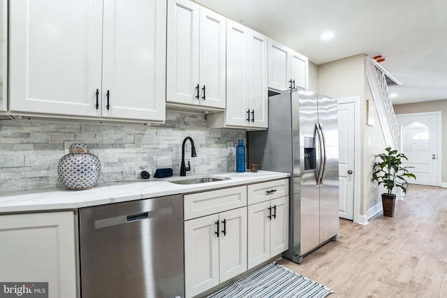 kitchen with light stone counters, light wood-style flooring, a sink, appliances with stainless steel finishes, and white cabinetry