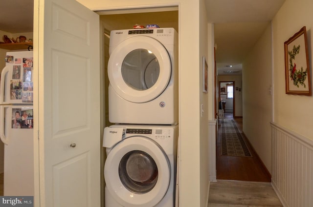 washroom featuring laundry area, wainscoting, wood finished floors, and stacked washer and dryer