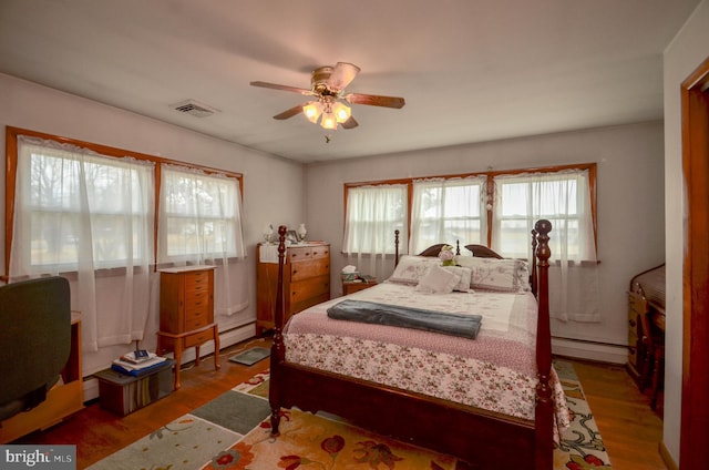 bedroom featuring a ceiling fan, wood finished floors, visible vents, and baseboard heating