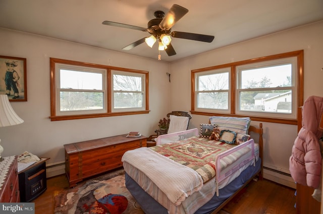 bedroom with multiple windows, wood finished floors, and baseboard heating