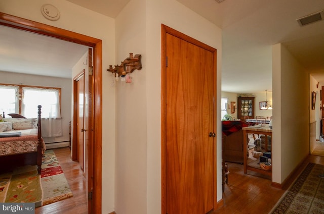 hall with visible vents, baseboards, baseboard heating, and light wood-style flooring