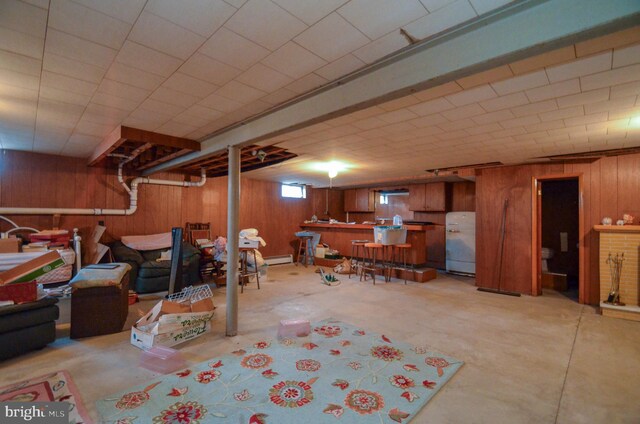 basement featuring wooden walls, a dry bar, a baseboard heating unit, and fridge