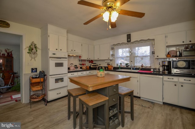 kitchen featuring dark countertops, light wood-style flooring, white appliances, and a sink