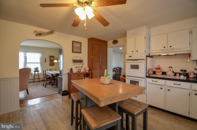 dining space with arched walkways, wainscoting, and light wood finished floors