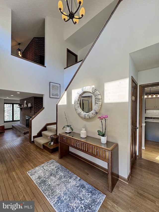 interior space featuring hardwood / wood-style floors, baseboards, a fireplace, a towering ceiling, and a notable chandelier