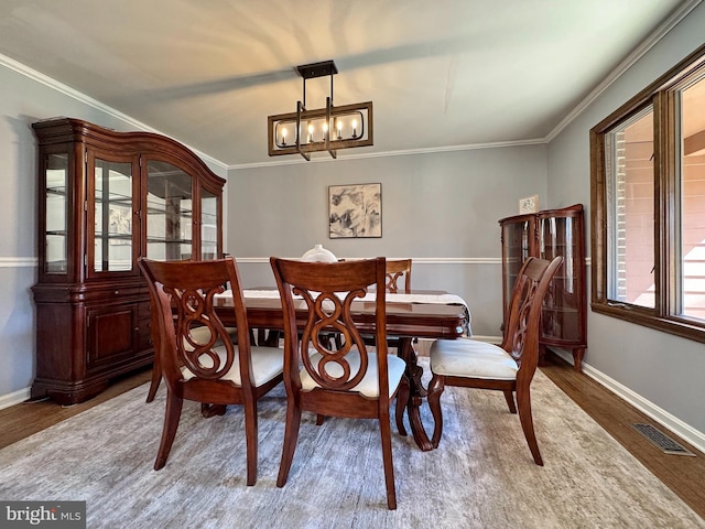 dining area featuring wood finished floors, baseboards, visible vents, crown molding, and a chandelier