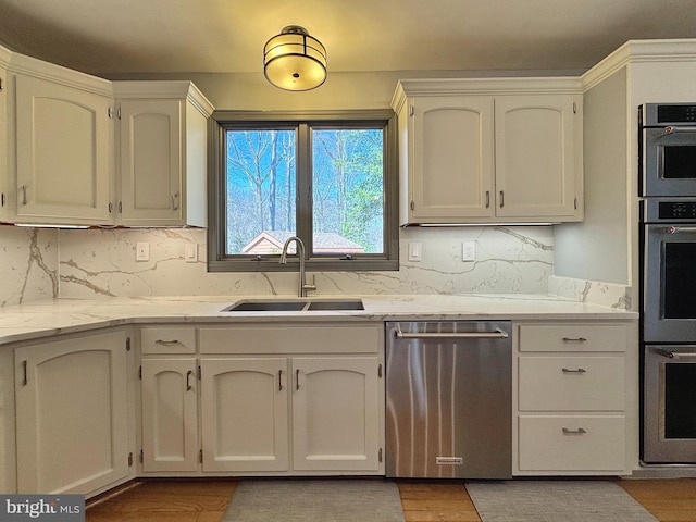 kitchen with light stone countertops, white cabinetry, a sink, decorative backsplash, and stainless steel dishwasher