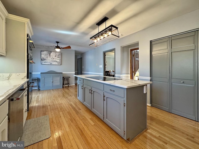 kitchen featuring gray cabinetry, a center island, black electric stovetop, light wood-style floors, and a ceiling fan