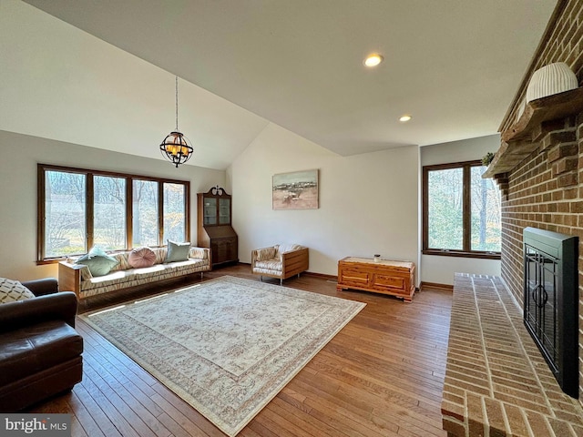 living area featuring a wealth of natural light, wood-type flooring, a brick fireplace, and vaulted ceiling