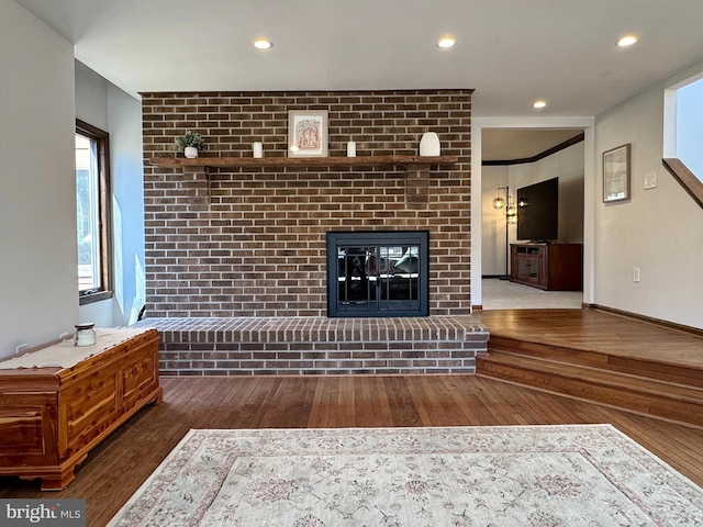 living area featuring a brick fireplace, recessed lighting, wood finished floors, and baseboards