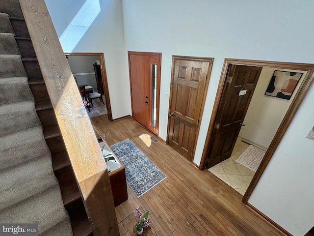 corridor featuring visible vents, baseboards, stairs, light wood-style flooring, and a high ceiling