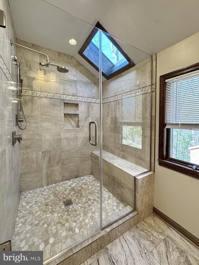 bathroom featuring baseboards, vaulted ceiling with skylight, marble finish floor, and a stall shower