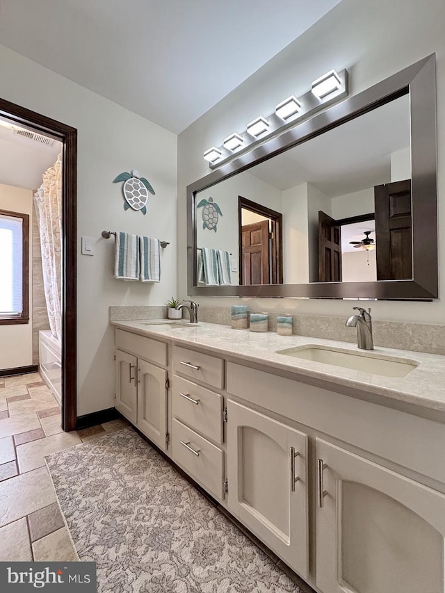 bathroom featuring double vanity, stone tile floors, baseboards, and a sink