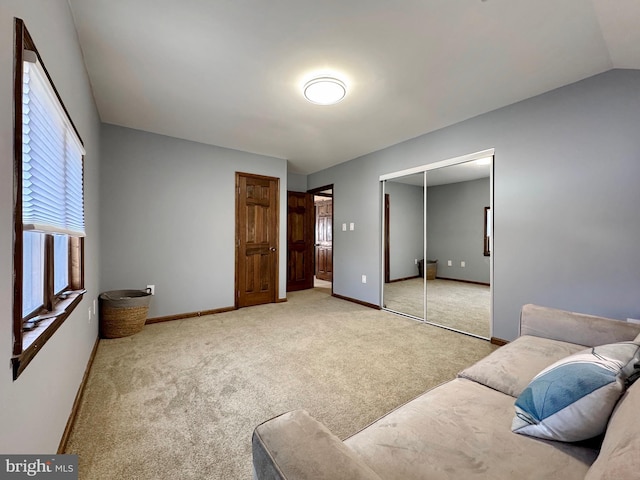 bedroom featuring a closet, light carpet, lofted ceiling, and baseboards