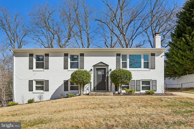 split foyer home featuring brick siding, a chimney, a front lawn, and fence