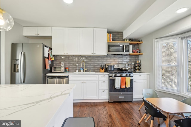 kitchen with dark wood-type flooring, decorative backsplash, appliances with stainless steel finishes, white cabinetry, and a sink