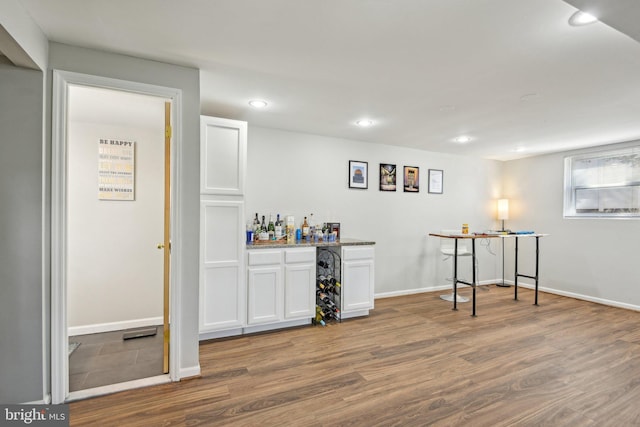 bar featuring recessed lighting, baseboards, a bar, and wood finished floors