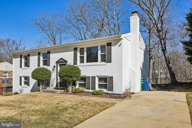 bi-level home with a front lawn, fence, brick siding, and a chimney