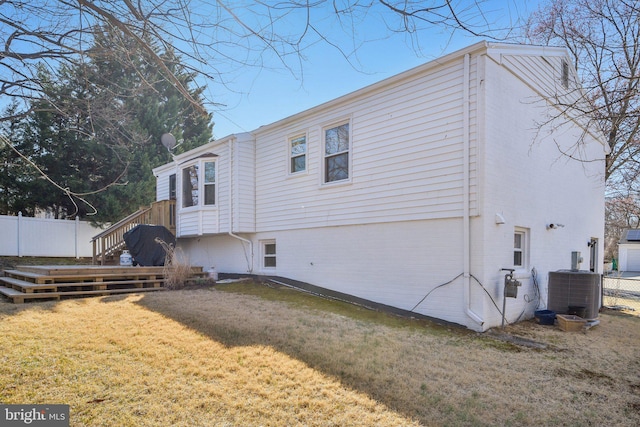 rear view of house with brick siding, central air condition unit, fence, and a lawn