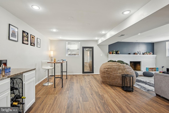 living room featuring a brick fireplace, wood finished floors, visible vents, and a wealth of natural light