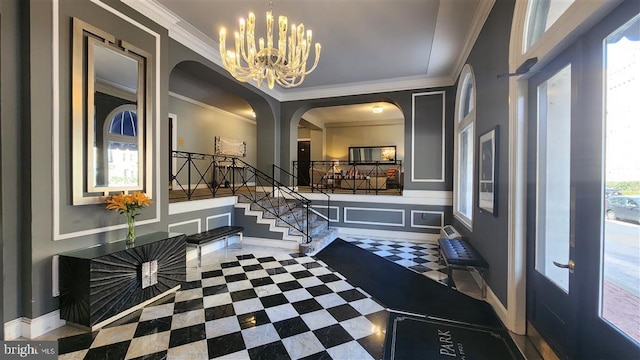 foyer entrance featuring a notable chandelier, ornamental molding, a decorative wall, baseboards, and stairs