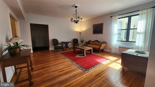 living area featuring an inviting chandelier, an AC wall unit, baseboards, and wood-type flooring