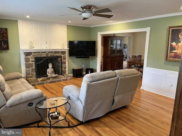 living room featuring a wainscoted wall, a fireplace, light wood-style floors, and ornamental molding